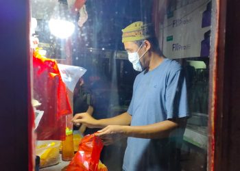 Agus, pedagang makanan di belakang pekong pasar sedang mengemas makanan pesanan konsumen