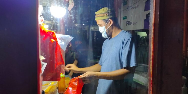 Agus, pedagang makanan di belakang pekong pasar sedang mengemas makanan pesanan konsumen